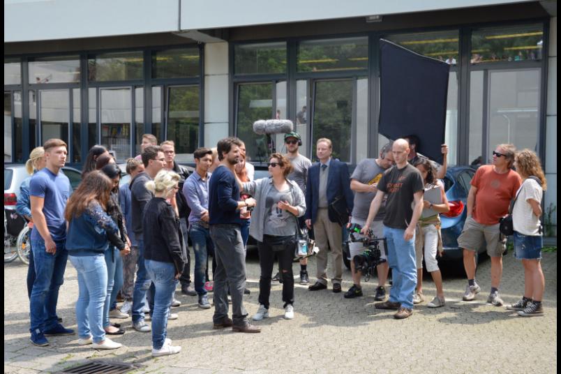 Tom Beck und Komparsen stehen an einem Filmset auf dem Campus.