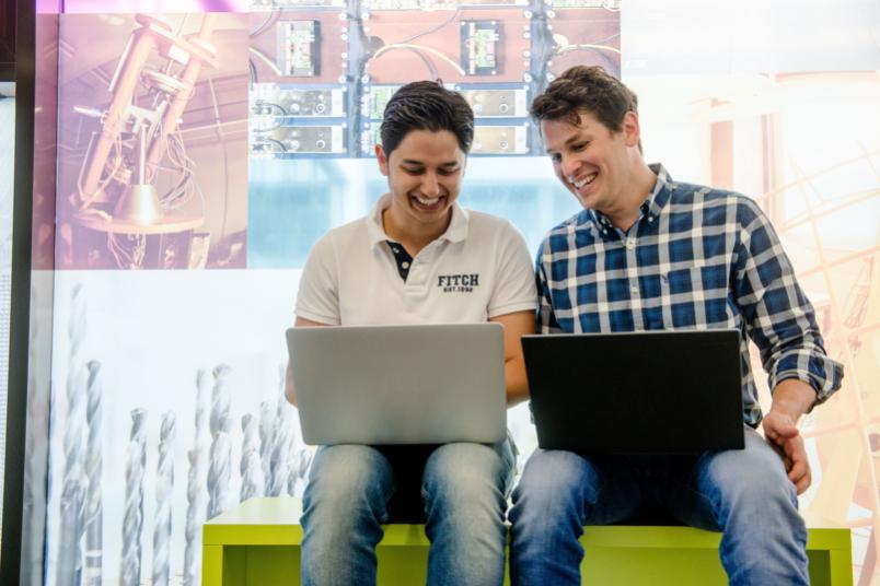 Zwei Männer lachen und haben ihre Laptops auf dem Schoß