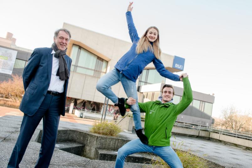 Rektor Schölmerich steht neben den Eiskunstläufern, die auf dem Campus eine artistische Hebefigur machen.