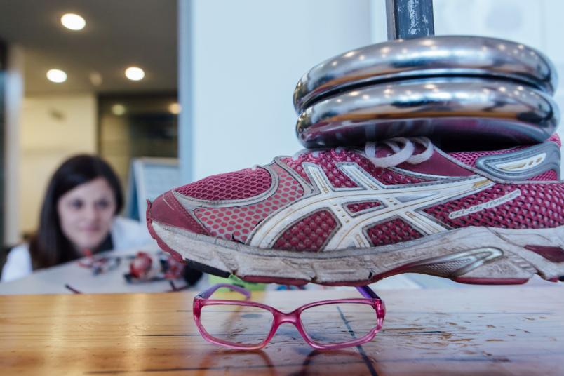 Eine Schulsportbrille wird getestet, indem sie unter ein Gewicht gelegt wird, dem sie standhalten soll.