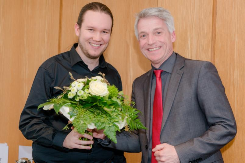 Zwei Männer, einer überreicht dem anderen Blumen
