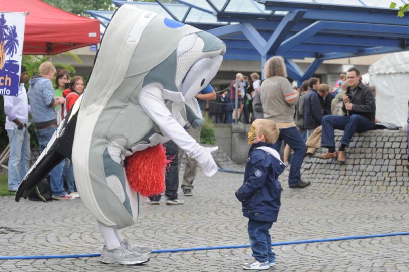 Eine Turnschuh-Maskottchen reicht einem als Tiger bemalten Kind die Hand.