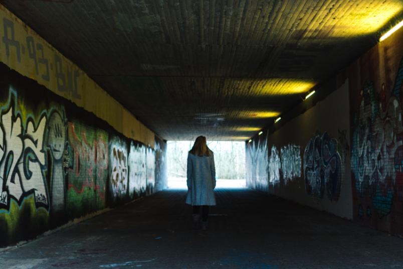 Eine Frau ist von hinten in einem dunklen Fußgängertunnel zu sehen.
