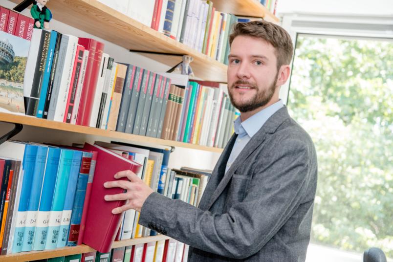 Wissenschaftler holt Buch aus einem Bücherregal.