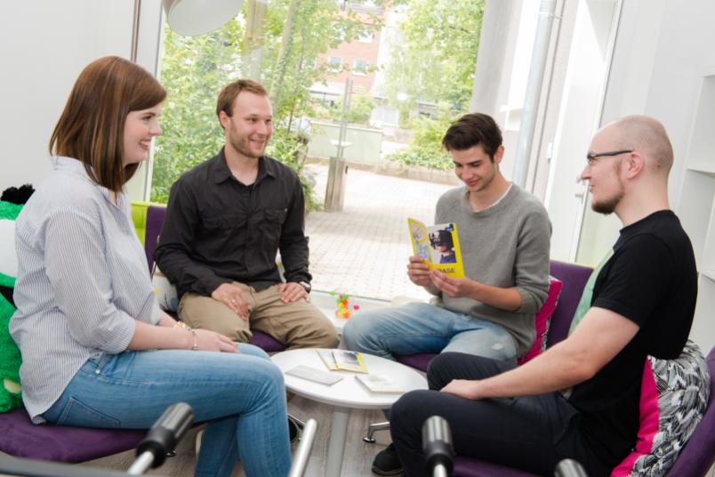 Vier Studierende sitzen in einem Stuhlkreis und unterhalten sich lachend.