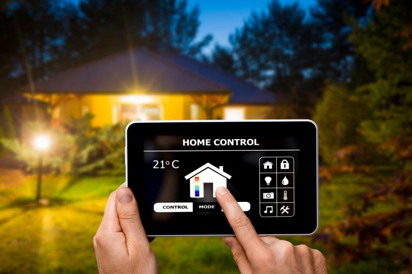 Eine Hand steuert mit einem Tablet Technik in einem Haus im Hintergrund.