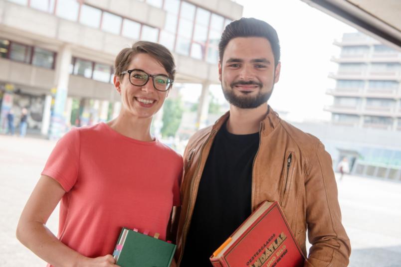 Zwei Studierende stehen nebeneinander mit Büchern in der Hand. 