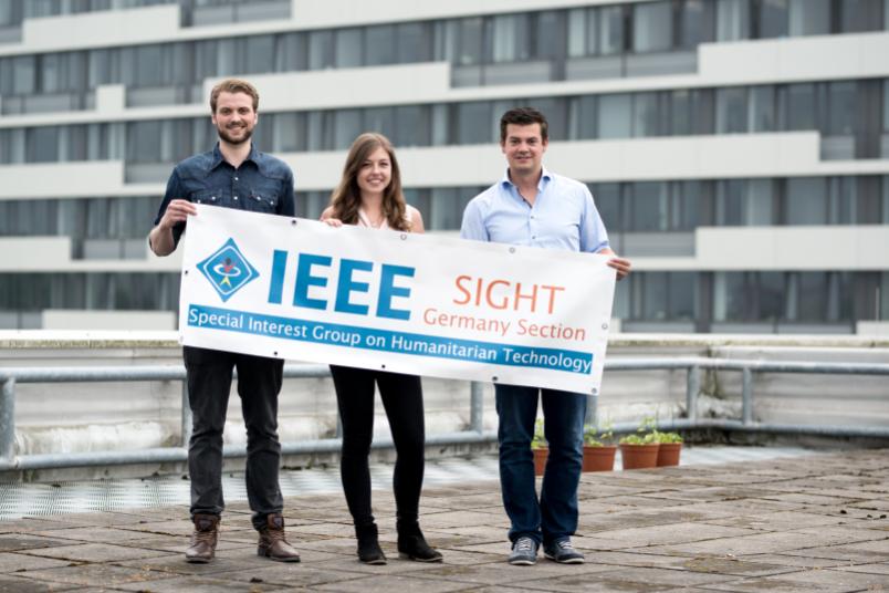 Drei Personen präsentieren ein Banner