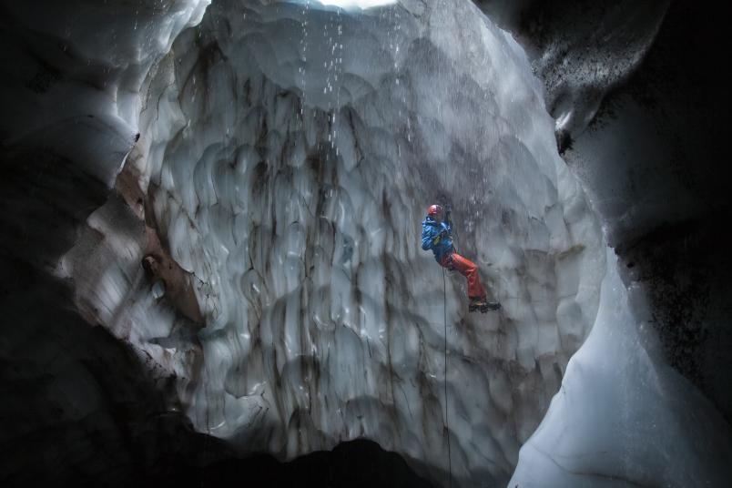Ein Mann seilt sich in eine Eishöhle ab.