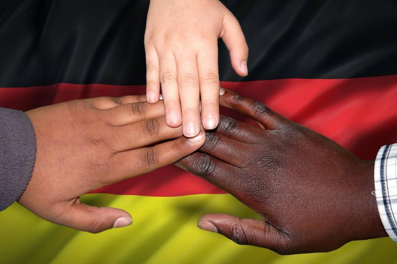 Integration: Drei verschieden farbige Hände liegen auf der Deutschlandflagge