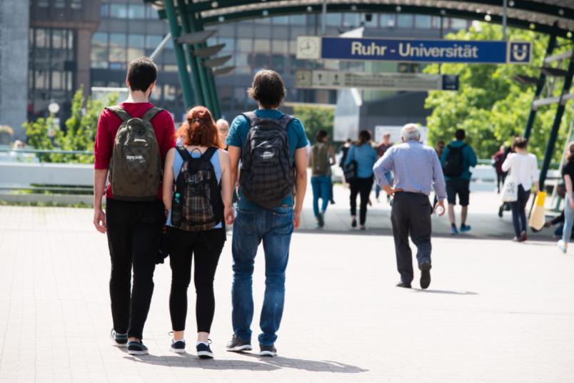 Drei Personen laufen auf der Unibrücke Richtung Haltestelle.