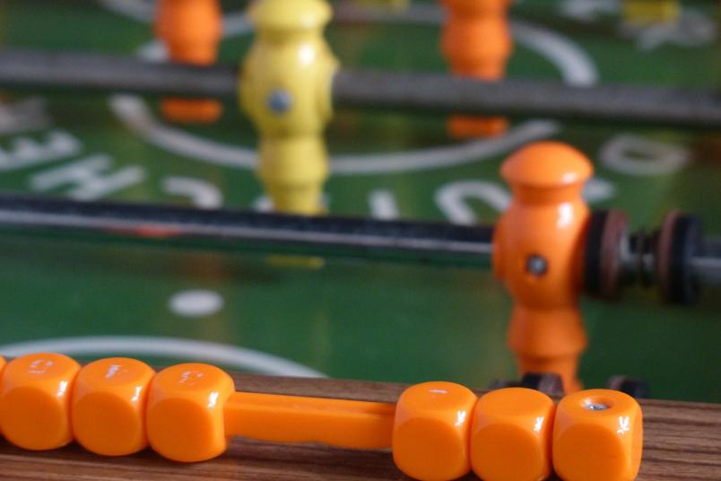 Gelbe und orangene Tischfußballfiguren in einem Kickertisch.