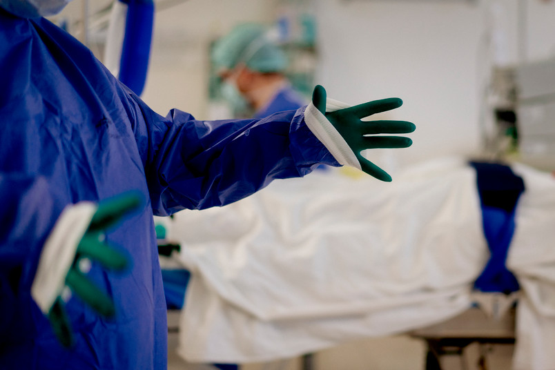 Blick in einen Operationssaal, in dem sich jemand Handschuhe und Kittel anzieht