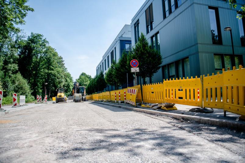 Die Asphaltdecke einer Straße ist abgetragen, im Hintergrund stehen Baufahrzeuge.
