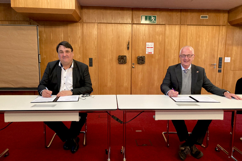 Zwei Männer sitzen am Tisch und unterzeichnen das Abkommen.