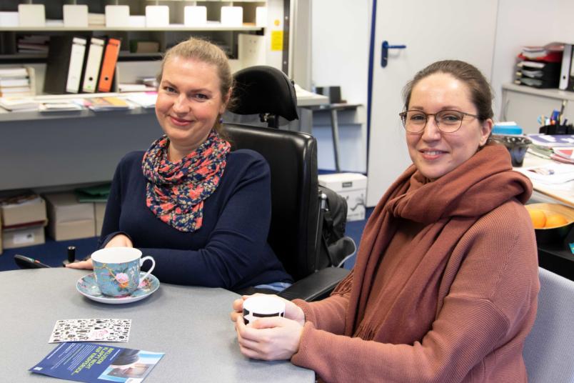 Zwei Frauen sitzen an einem Tisch nebeneinander.