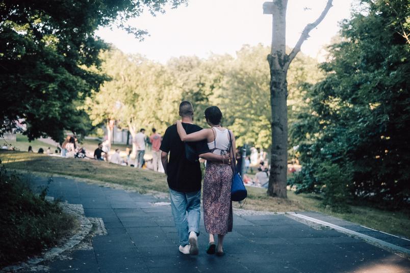 Zwei Menschen laufen Arm in Arm unter Bäumen her