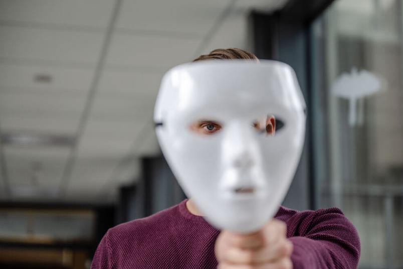 Mann hält eine weiße Theatermaske. 
