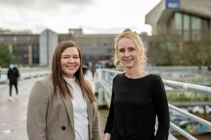 Die neuen Gleichstellungsbeauftragten der RUB, Dr. Wanda Gerding (links) und Nadine Müller, stehen gemeinsam auf der Unibrücke. Im Hintergrund ist ein Teil des Campus zu sehen.