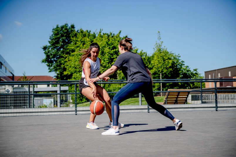 Zwei Studentinnen spielen draußen Basketball.