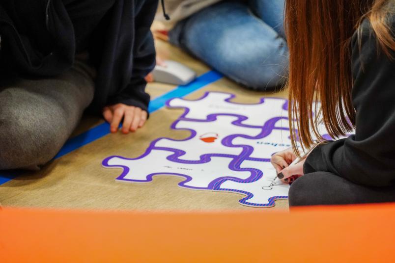 Schülerin schreibt etwas auf ein großes Puzzleteil. 