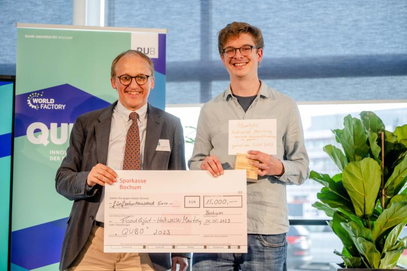 Der Prorektor Prof. Dr. Günther Meschke und der Award Gewinner Dr. Benjamin Mewes stehen auf der Bühne und halten den Check mit dem Preisgeld lächelnd hoch. 