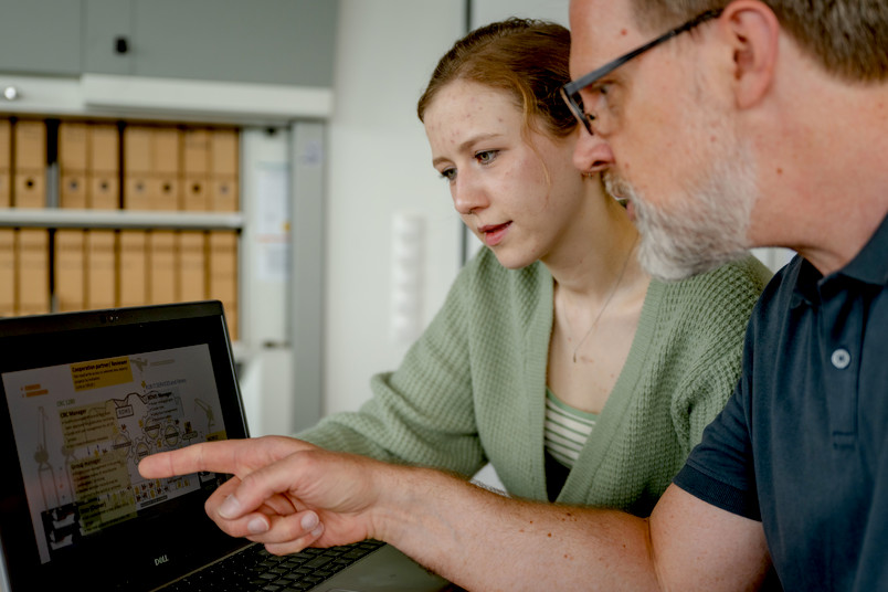 Mann zeigt junger Frau etwas auf Laptopbildschirm