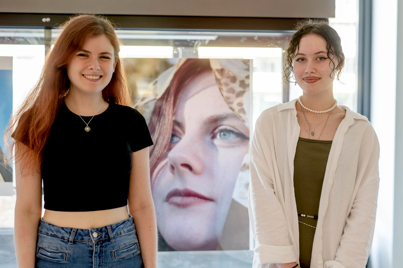 Zwei Studentinnen vor Schaukasten mit Foto: Ellen Fast (rechts) und ihre Schwester Milena