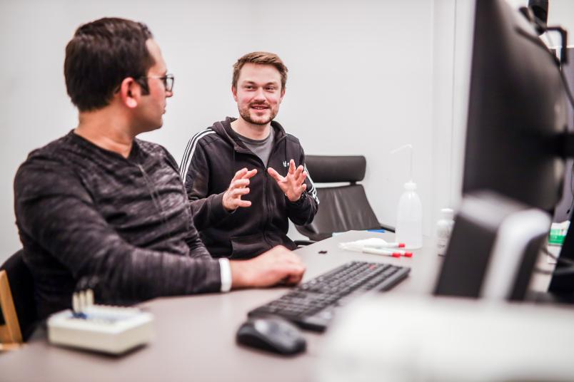 Zwei Personen sitzen vor einem Computer und sprechen