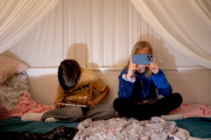 Zwei Kinder mit Tablet und Smartphone auf einem Bett