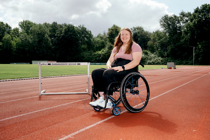 Lisa Clemens steht mit ihrem Rollstuhl auf einer Tartanbahn. 