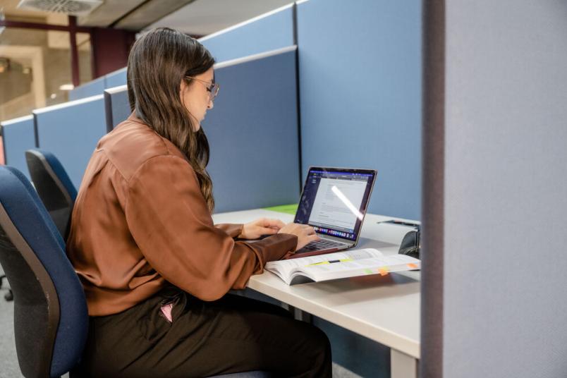 Studentin sitzt an einem Schreibtisch und schreibt auf dem Laptop. 