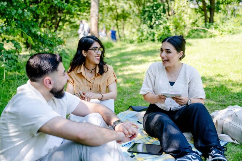 Studierende sitzen auf einer Wiese und unterhalten sich. Es scheint die Sonne.