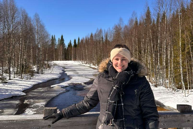 Studentin steht in Winterkleidung vor einem Fluss auf einer Brücke