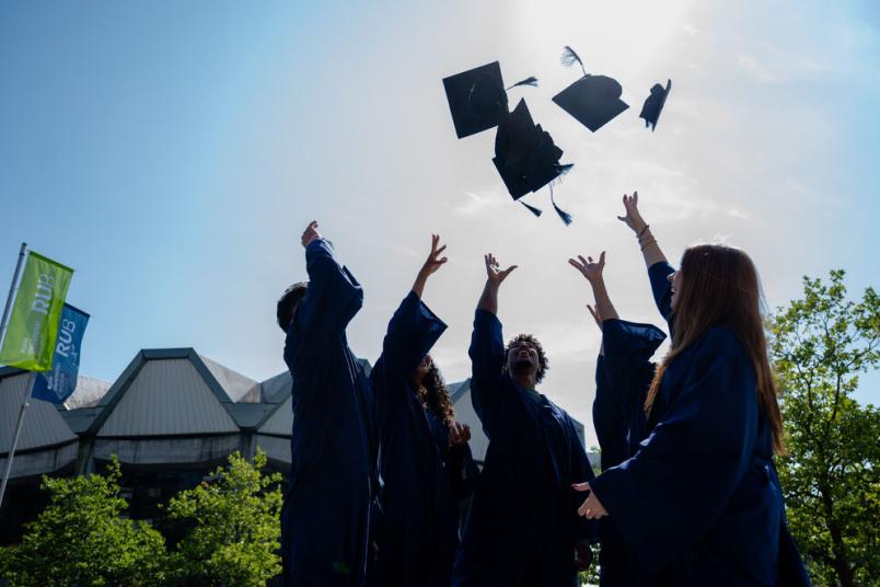 Studierende werfen Doktorhüte in die Luft.