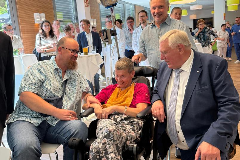 Minister Laumann kniet neben einer Patietin im Rollstuhl