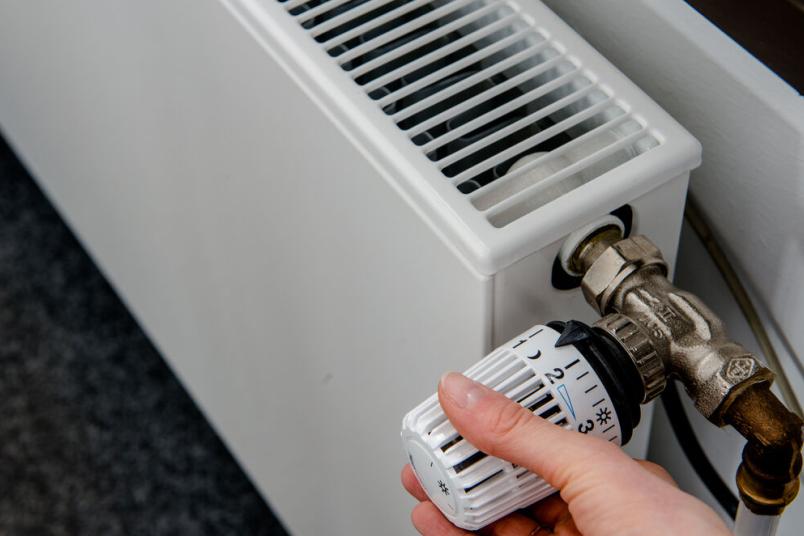 Eine Hand am Thermostat eines Heizkörpers