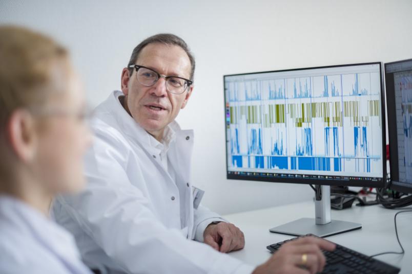 Ein Mann und eine Frau im weißen Kittel sitzen vor einem Monitor mit Grafiken