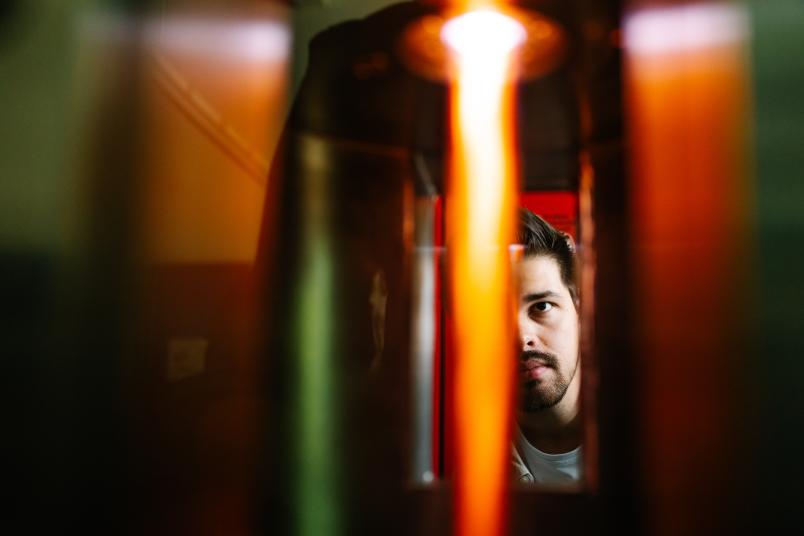 In einem Reaktor leuchtet eine rote Gasflamme, im Hintergrund ist eine Person zu sehen