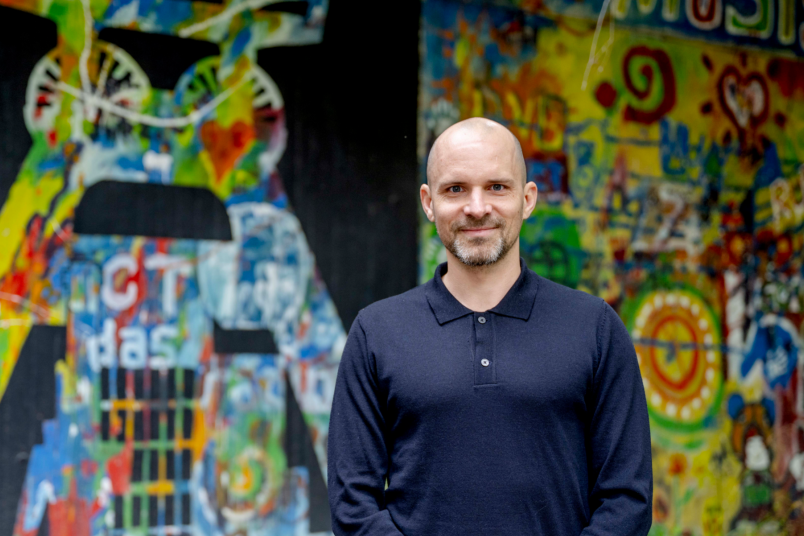 Ein Mann in einem blauen Pullover vor einer bunt bemalten Wand