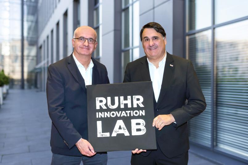 Porträt der Rektoren Manfred Bayer und Martin Paul mit einer Leinwand, auf der das Ruhr-Innovation-Lab-Logo zu sehen ist
