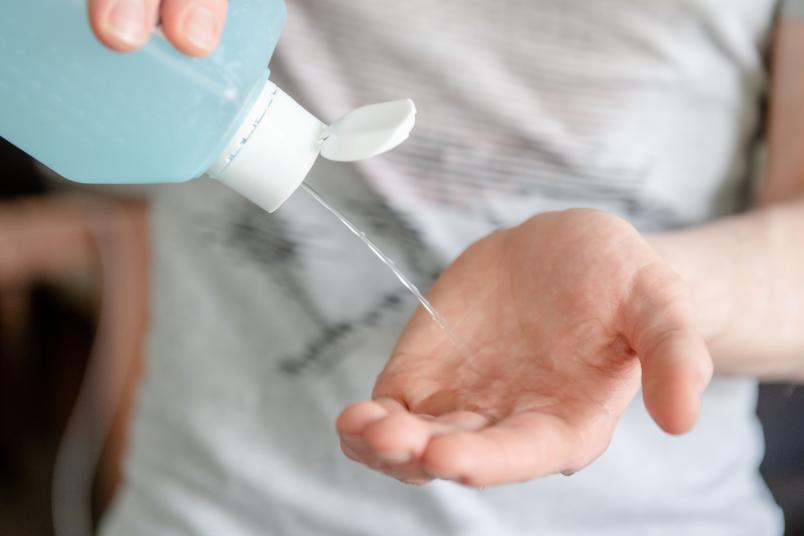 Jemand schüttet Desinfektionsmittel aus einer Flasche in seine Hand