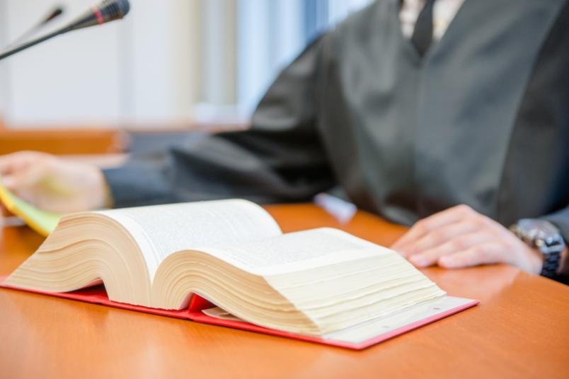 Ein Gesetzbuch liegt aufgeschlagen vor einer Person in Robe auf einem Tisch