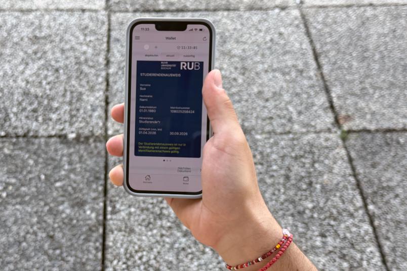 Eine Hand hält ein Smartphone. Auf dem Bildschirm ist der digitale Studierendenausweis.
