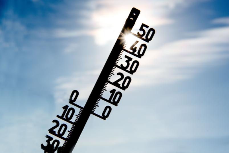 Thermometer vor blauem Himmel und Sonne