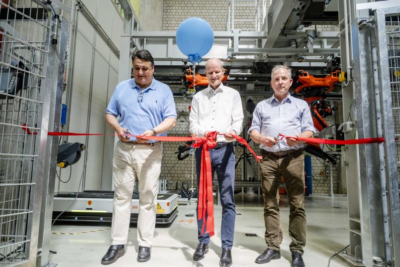 Drei Männer mit Scheren schneiden ein rotes Schleifenband durch