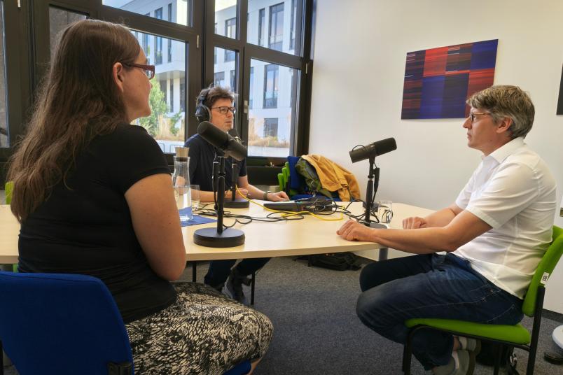 Drei Personen am Tisch vor Mikrofonen