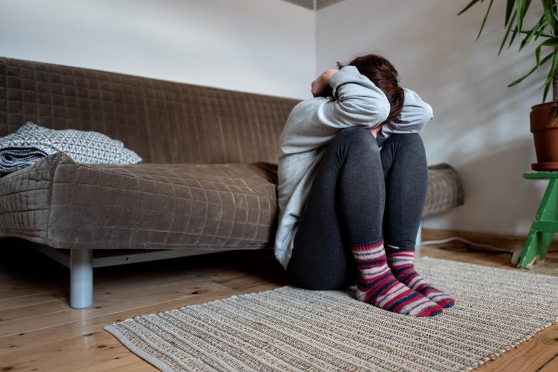 Eine Frau, die den Kopf zwischen den Armen hat und vor einem Sofa hockt