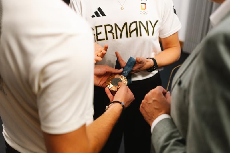 Männer und Frauenhände halten eine olympische Medaille