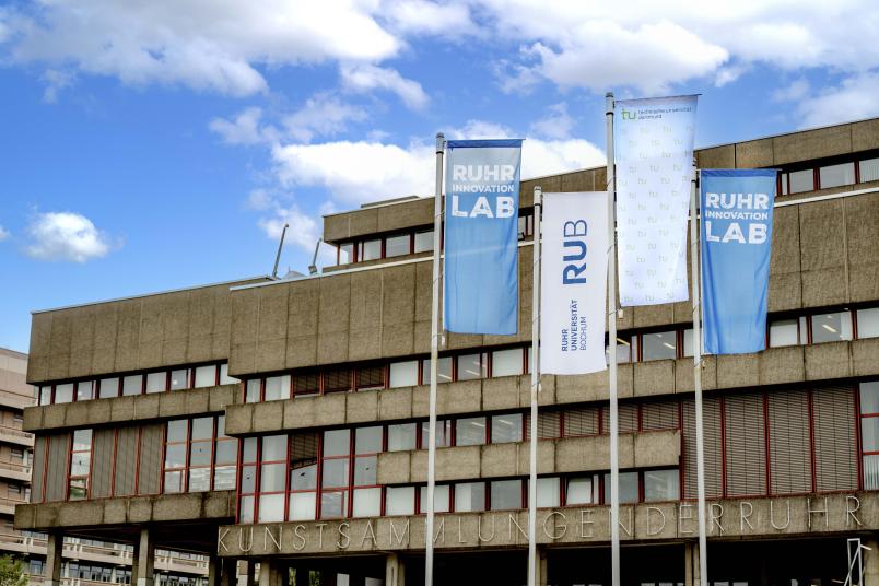 Flaggen der RUB, der TU Dortmund und des Ruhr Innovation Lab vor der Universitätsbibliothek
